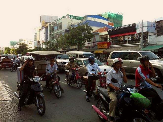 Phnom Penh traffic, including tuk tuks, SUVs and moto drivers busy driving and texting.