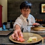 A Cambodian sushi chef putting a single piece of nigiri sushi onto a plate.