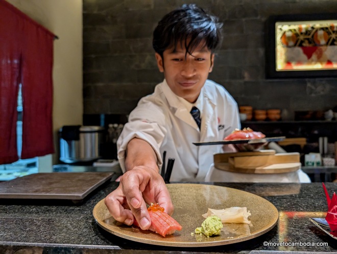 A Cambodian sushi chef putting a single piece of nigiri sushi onto a plate. 